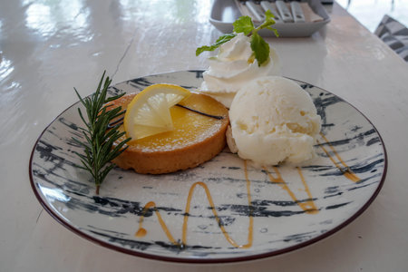 lemon tart with vanilla ice cream on cute round plate in cafeの写真素材