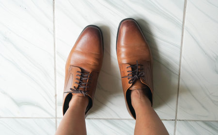 top view of woman feet wearing oversize brown men leather shoes
