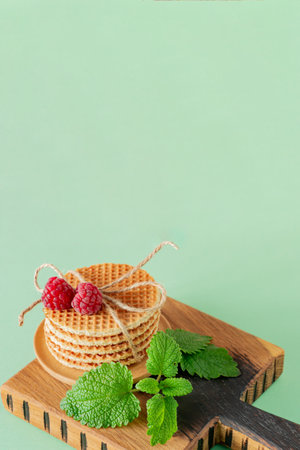 Pile of caramel round Dutch waffles with raspberries and melissa leaves on cutting board and blue background with copy space.の写真素材