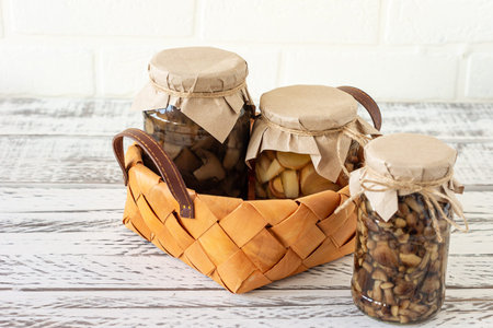 Glass jars with canned mushrooms in a basket. Fermented food on a white background with copy space.