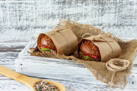 Healthy breakfast - burger with smoked salmon, salad leaves and avocado served in a craft paper on wooden background, horizontalの写真素材