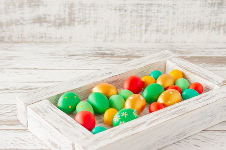 Colorful hand painted easter eggs in white wooden box on wooden table with copy spaceの写真素材