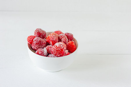 Frozen strawberry in white bowl on a wooden table. berries covered with hoarfrost.の写真素材