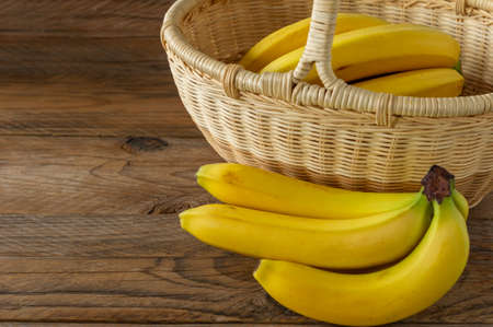 Rip bunch of bananas in wicker basket on wooden background. Healthy eating concept.の写真素材
