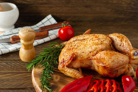 Whole roasted chicken on a wooden bord served with fresh vegetables and herbsの写真素材
