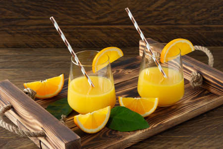 Fresh orange juice in glasses with cut oranges on wooden tray. Rustic still life with citrus fruits.の写真素材