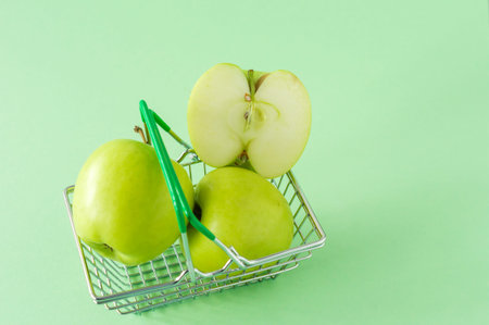 Ripe green apples on shopping toy basket on green background. Concept ofr grocery or market with...