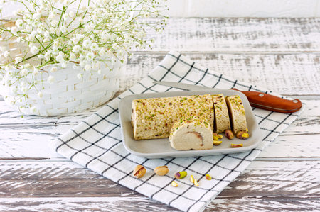 Sliced tahini halva with pistachio on a white wooden desk decorated with flowers