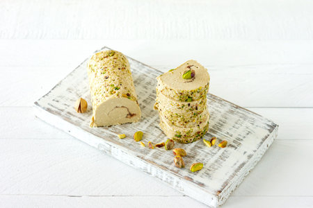 Halva with pistachio served on white wooden desk with flowers.