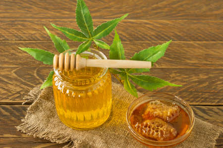 glass jar of honey, wooden dipper and hemp leaves close-up on wooden background. CBD healthy products. Sweet dessert. Alternative medicine.の写真素材
