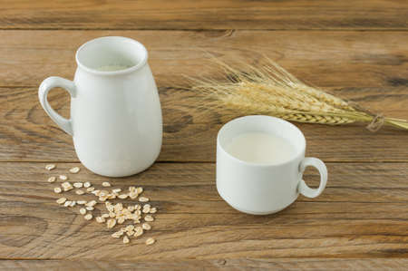 Oat milk in white pitcher and oatmeal in a cup on a wooden tableの写真素材