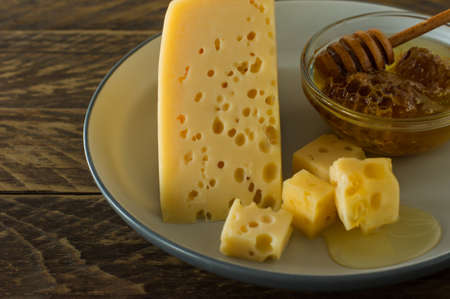 Radamer cheese on a plate served with honey. triangular piece of yellow cow's milk swiss cheese with holes.の写真素材
