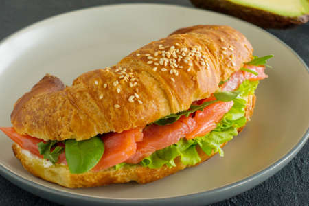 croissant sandwich with salmon, ricotta cheese and arugula on a plate on a dark background. Side view close up.の写真素材