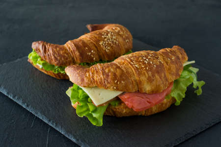 Croissant sandwiches with salted salmon on a desk, served with fresh salad leaves, arugula and vegetables over black background.の写真素材