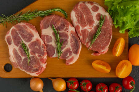 Raw pork steakes - ready for cooking with herbs and tomatoes. wooden background.の写真素材