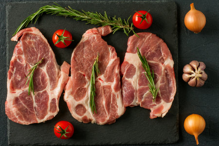Food organic Fresh Crude Pork Neck on black slate stone with rosemary, onion amd tomatoesの写真素材