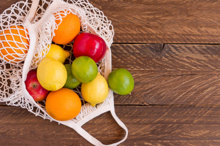 Organic fruits assorted in cotton mesh on wooden table, reusable shopping bag. sustainable lifestyle...