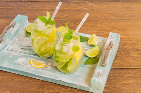 summer fresh cold lemonade with lime, lemon, mint and ice served on blue wooden tray. Non-alcoholic...