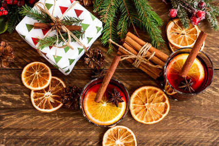 Glasses with Hot red mulled wine for winter and Christmas with orange slice, anise and cinnamon stick decorated with fir branches and wrapped presents for holidays. Festive greeting card.の写真素材