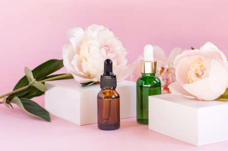 Serum glass bottles with pipette and beautiful peony flower on pastel pink background. Natural Organic Spa Cosmetic concept. Front viewの写真素材