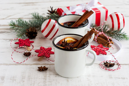 Mulled wine in white enameled mugs with spices and citrus fruit on wooden table with fur tree branches and christmas presentsの写真素材