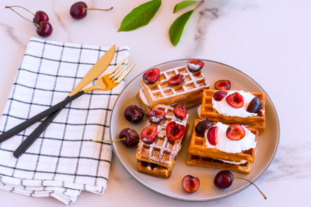 homemade belgin waffles whith whipped cream and cherries served on a plate for breakfast.の写真素材