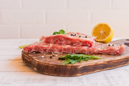 Fresh pork ribs, meat marinated and prepared for roast with spices and lemon on wooden background...