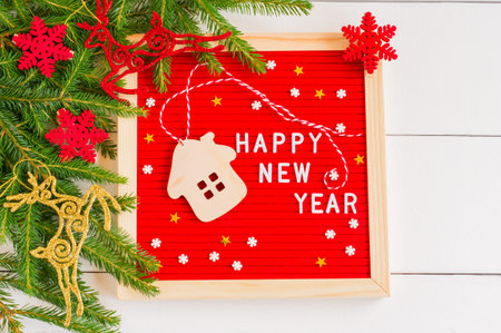 Red felt letter board with text happy new year and white wooden toy house and sugar sprincles on...