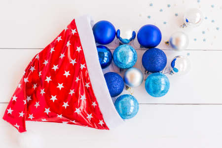 Top view of red and white santa cap with scatteredblue and silver baubles for christmas tree decoration. Festive greeting card for winter holidays.の写真素材