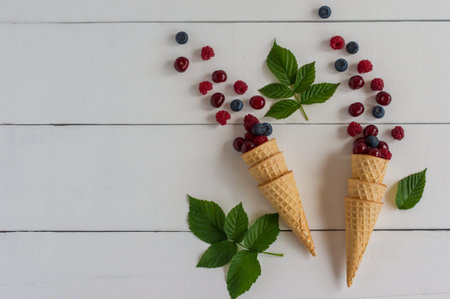 Fresh blueberry, cherry and raspberry in waffle cone on wooden white background. Top view.
