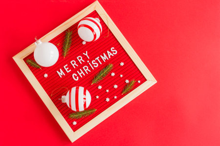 Merry Christmas text made with white letters on a red wooden board with baubles, fir tree brabches...