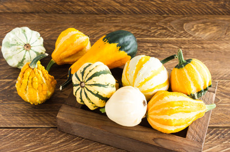 autumn decorative pumpkins of different shapes and colors in a box on a wooden background