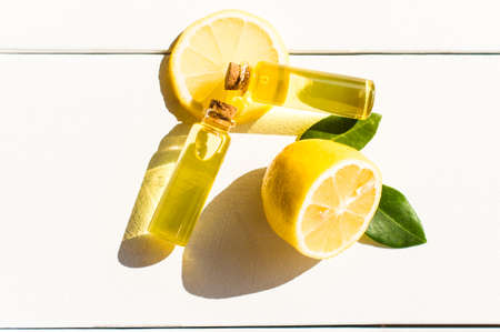 two transparent bottles with a cork lid with aromatic lemon oil on a white wooden table. sezhiy lemon and green leaves. sunlightの写真素材