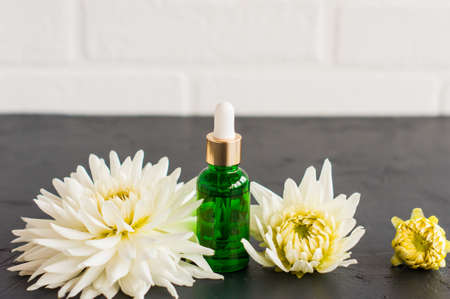 moisturizing serum in a cosmetic bottle with a pipette made of green glass against the background of a white brick wall and flowersの写真素材