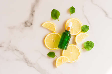 moisturizing lemon oil in a bottle with a pipette against the background of slices of juicy lemon and fresh mint leaves. top viewの写真素材