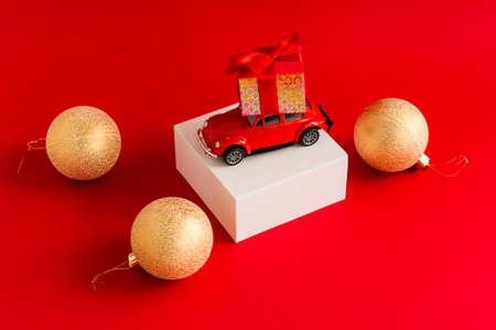 Red retro car with a gift box on the roof on a white podium and a red background with a new-fashion ball. a copy of the spaceの写真素材