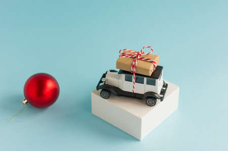 a retro car model with a Christmas box on the roof on a white podium and a blue background with a red Christmas ballの写真素材