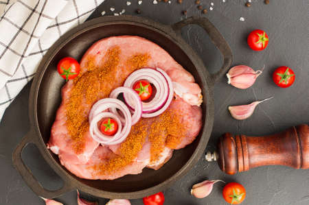 top view of the pan with raw chops of selected pork meat with spices, onions, garlic and fresh tomatoesの写真素材