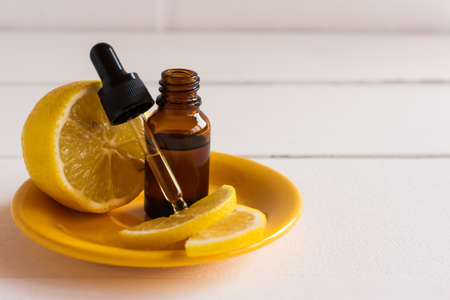 serum with lemon extraty for facial skin care in a glass flaon with a pipette and lemon fruit on a yellow plateの写真素材