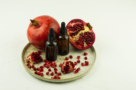 two glass cosmetic bottles with a dropper on a ceramic plate with pomegranate fruit. the concept of beauty, facial skin care. white backgroundの写真素材