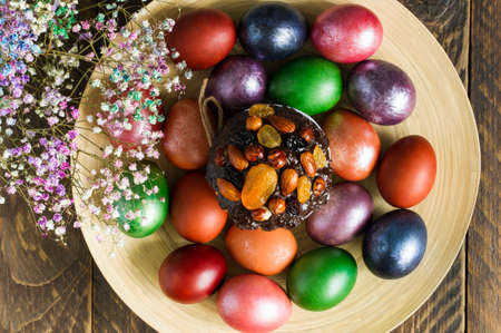 top view of a plate with an Easter cake and painted bright eggs. spring flowers. wooden backgroundの写真素材