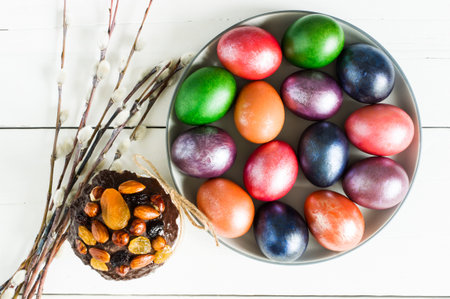 top view of a large plate with Easter multi-colored eggs and willow twigs. white wooden background