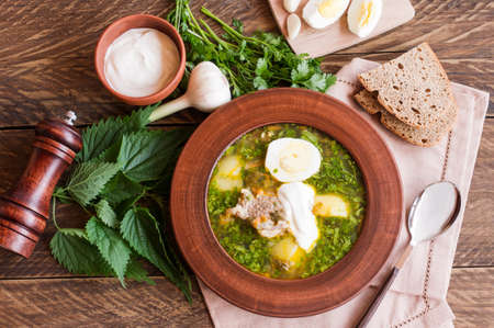 brown ceramic plate with sorrel and nettle soup on steamed pork broth with garlic and cilanta on a wooden background. top viewの写真素材