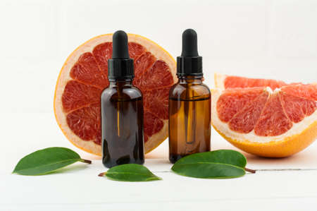two bottles of droppers with cosmetic grapefruit oil or facial serum against the background of fresh grapefruit fruit. a natural concept of self-careの写真素材
