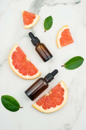 flat layout. two bottles of droplets with grapefruit oil and slices, leaves on a marble white background. top viewの写真素材