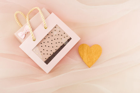 Gift box in a beautiful pink bag on a pastel background veil with a heart of gold. A gift with love
