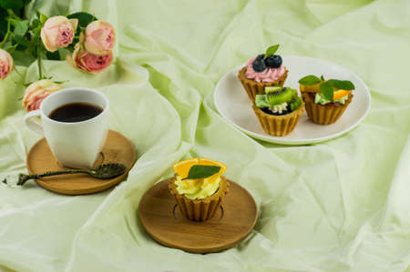 a cup of coffee and mini tortillas with cream and fresh fruit on a plate. delicate pastel background with a bouquet of rosesの写真素材