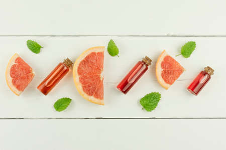 glass bottles with a lid with cosmetic organic grapefruit and lemon balm leaves on a white wooden background. top view. flat layの写真素材