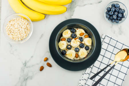 healthy homemade oatmeal porridge in a dark bowl with slices of ripe banana and blueberries. almonds to improve the vkua. top view. marble tableの写真素材