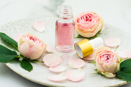 an open bottle of rose oil and a pipette filled with cosmetics for rejuvenation and facial skin care on a ceramic plateの写真素材